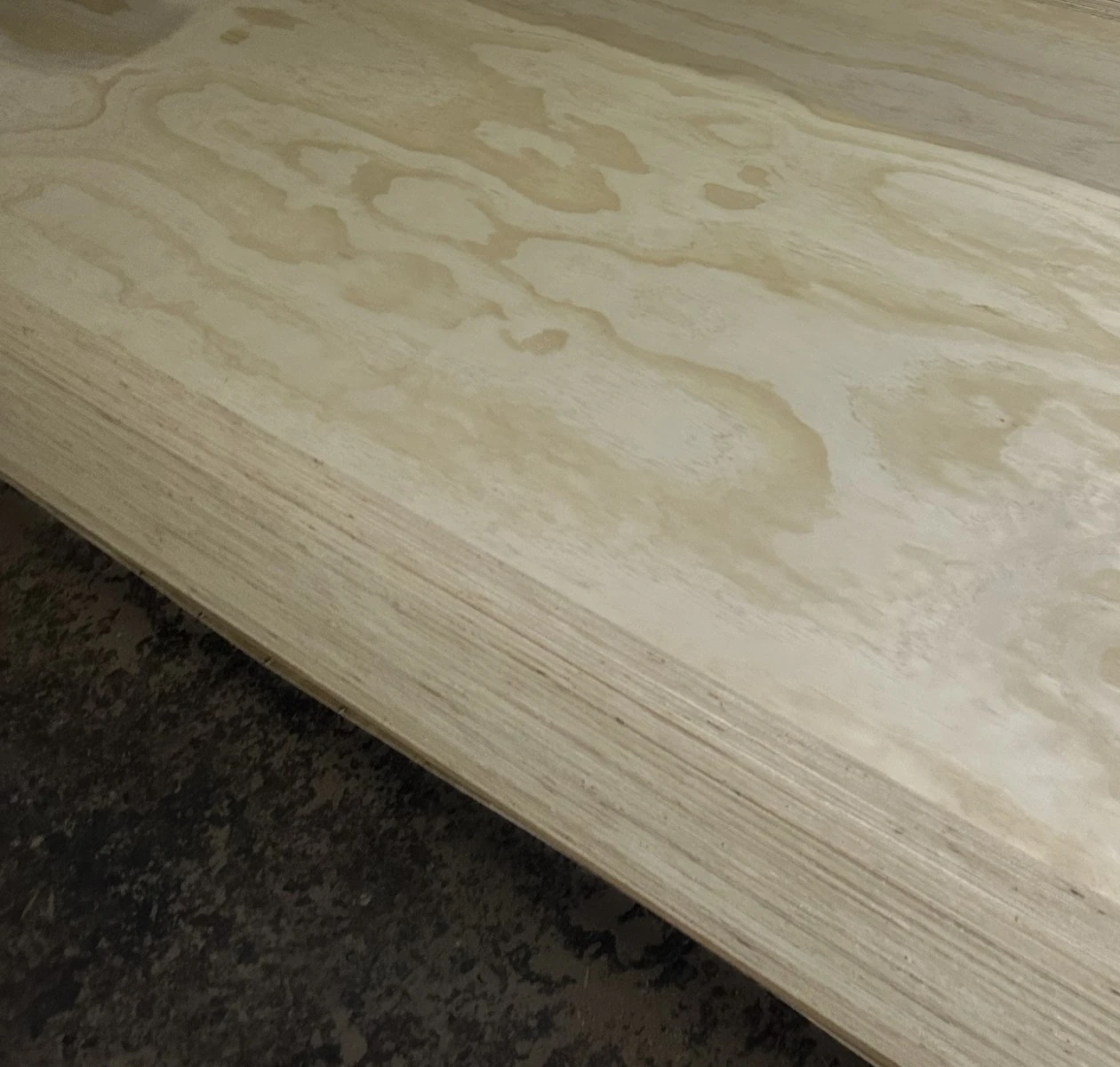 Pine-faced plywood sheet with honey cathedral grain lying on a pack, multi-ply edges visible